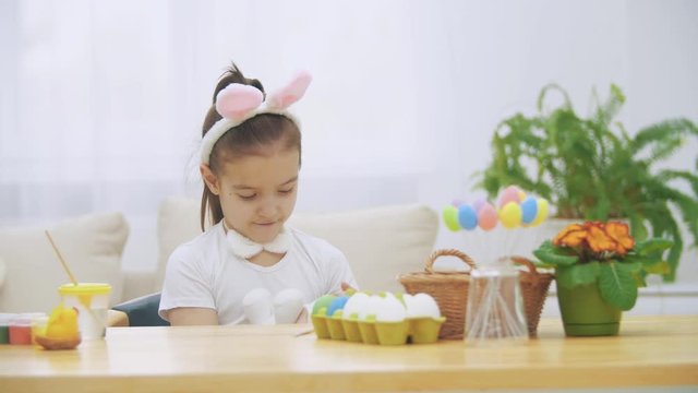 Nice, cute girl is having fun paiting with Easter bunny, Adorable girl is lulling bunny and cudding it. Girl with a beauty spot at her face and is smiling gently, sitting at the wooden table with