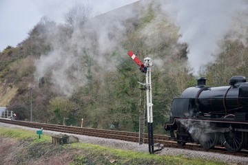 Fototapeta na wymiar Black steam train on railway line (track) under hill near signal post