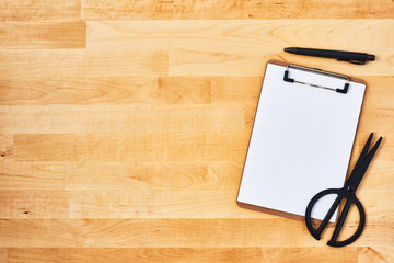 Cardboard clipboard, scissors and pen on yellow wood background. Top view. Copy space for text.