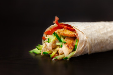 Shawarma sandwich - fresh roll of thin lavash (pita bread) filled with grilled meat, mushrooms, cheese, cabbage, carrots, sauce, green. Traditional Eastern snack. On a wooden background