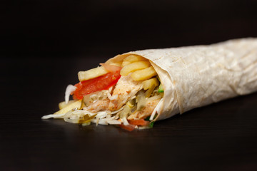 Shawarma sandwich - fresh roll of thin lavash (pita bread) filled with grilled meat, mushrooms, cheese, cabbage, carrots, sauce, green. Traditional Eastern snack. On a wooden background