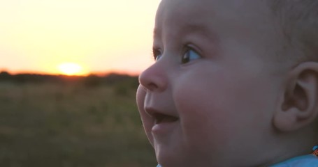 Happy baby smiling in a large field at sunset in summer in slow motion
