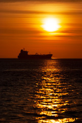 Fototapeta premium Freighter Ship At Sunset in the Puget Sound. As the sun sets over the horizon a freighter sails north in the Salish Sea area of western Washington state.