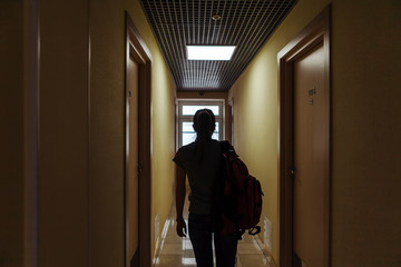 A young woman with a backpack is walking along the corridor of the hotel to her room. Silhouette of a girl with a backpack