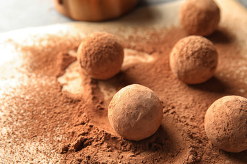 Sweet chocolate truffles powdered with cacao on parchment paper, space for text