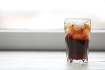 Glass of cola with ice near window, space for text