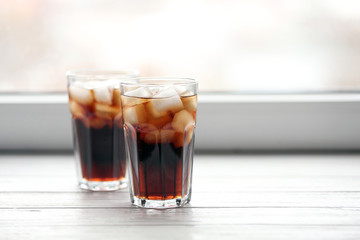 Glasses of cola with ice near window, space for text