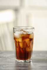 Glass of cola with ice on table against blurred background, space for text
