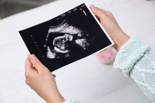 Woman holding ultrasound photo of baby over table, closeup