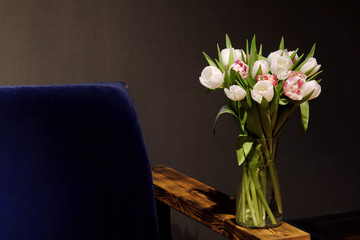 A bouquet of tulips of different colors, white, pink, stands in a glass vase in a dark interior.