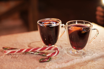 Glass cups of mulled wine and candy canes on table covered with snow outdoors. Space for text