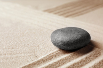 Fototapeta na wymiar Zen garden stone on sand with pattern, space for text. Meditation and harmony
