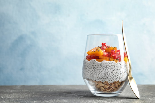 Glass of tasty chia seed pudding with granola, persimmon and pomegranate on table, space for text