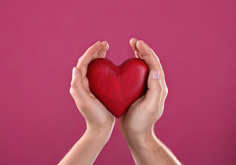 Man and woman holding decorative heart on color background, closeup