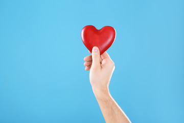 Obraz premium Man holding decorative heart in hand on color background