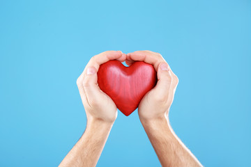 Man holding decorative heart in hands on color background, closeup
