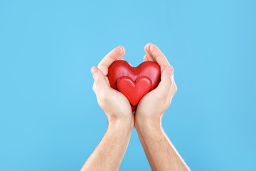 Man holding decorative hearts in hands on color background, closeup