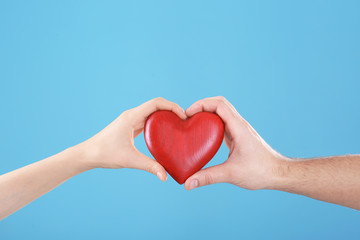 Man and woman holding decorative heart on color background, closeup