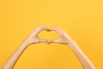 Fototapeta premium Woman making heart with her hands on color background, closeup
