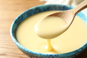 Spoon of pouring condensed milk over bowl on table, closeup. Dairy products