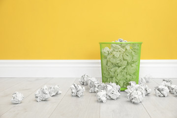 Metal bin with crumpled paper against color wall, space for text