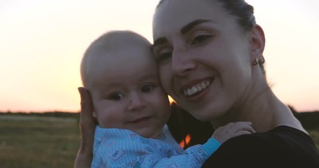 Optimistic mother and her baby in hands embracing each other at sunset in slo-mo