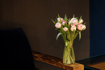 A bouquet of tulips of different colors, white, pink, stands in a glass vase in a dark interior.