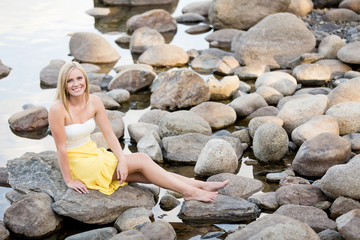 Attractive young woman sitting on river rocks