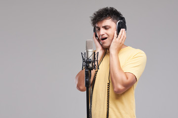 Portrait of rock singer man in studio professional headphones keeping static mic, sings a song...