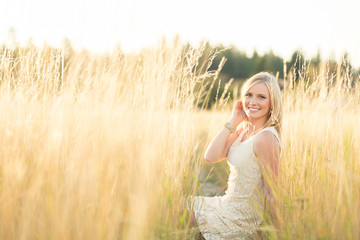 beautiful young lady sitting in field smiling