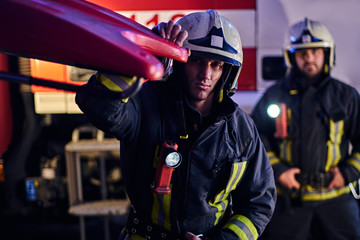 Two firemen wearing a protective uniform standing next to a fire truck. Arrival on call at night...