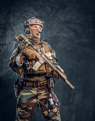 Elite unit, special forces soldier in camouflage uniform posing with assault rifle. Studio photo against a dark textured wall