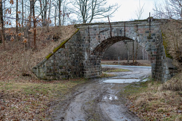 Stone viaduct over the old railway track. A dirt road leading under an old railway bridge.