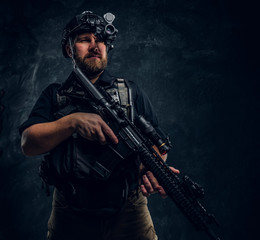 Bearded special forces soldier or private military contractor holding an assault rifle and observes...