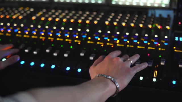 A man works in a recording studio on a mixing console. Hands close up