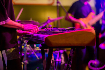 musician's hands playing keyboard at a live show on stage with other men playing guitars, the...