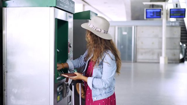 Woman passanger standing near cash machine inside modern tranportation terminal and charging travel pass