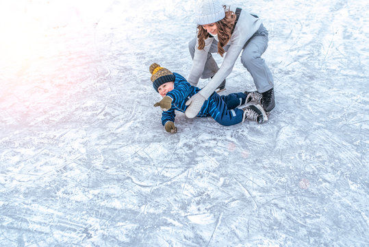 The baby fell on the ice. A young mother skates in the park in winter, with her son a young child 3-5 years old. Weekend rest at a public skating rink, happy smiling.