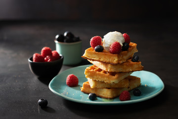 Freshly baked waffles with raspberries, berries, honey and coffee for breakfast or brunch on a dark background with copy space. Homemade Dessert concept.