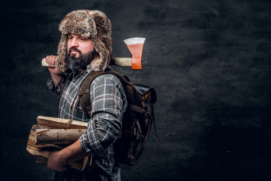 Brutal woodcutter with firewood and ax. Studio photo against a dark textured wall