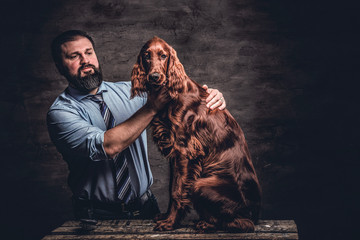 Middle-aged hunter shows his well-groomed purebred English Setter who sitting on a wooden pedestal....