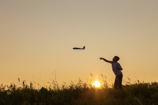 Black silhouette of happy caucasian child boy playing with toy airplane outside in meadow on sunny sunset time. Dreaming, imagination, curiosity concept. Horizontal color photography.