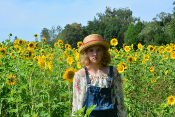 Mädchen mit Hut steht vor einem Sonnenblumen Feld 