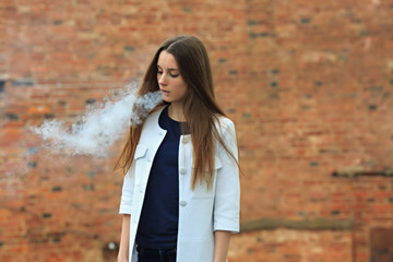 Vape teenager. Young pretty white girl in white cardigan smoking an electronic cigarette opposite...