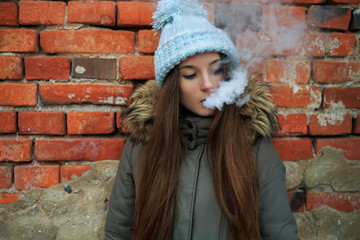 Vape teenager. Young pretty white girl in blue cap and green jacket smoking an electronic cigarette...