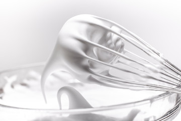 Metal whisk with whipped egg whites on white background
