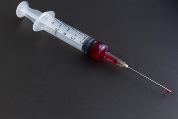 Medical syringe with needle and blood isolated on black and green background.