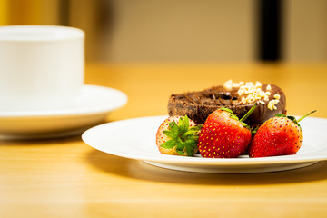 Chocolate donuts and strawberries on a white plate.