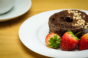 Chocolate donuts and strawberries on a white plate.