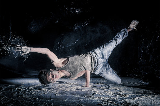 cool dirty сhinese  guy dancer in style of bboying doing complex tricks on floor in Studio filled with flour on black background. concept of space dance on surface of planet moon